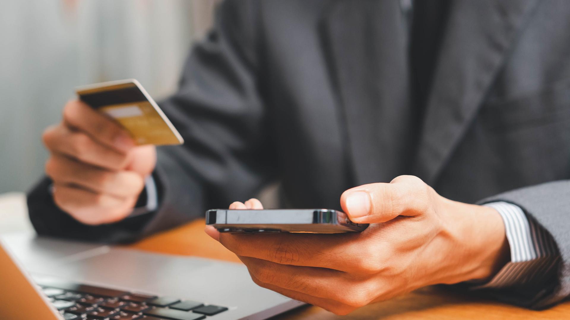 Smarter Software Software Lösungen im Finanzwesen | © AdobeStock_964418585 Mann im Anzug sitzt mit Smartphone und Kreditkarte in den Händen am Laptop